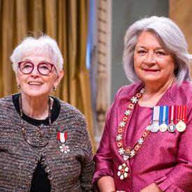 Governor General Simon is standing next to a woman who has a medal pinned to her brown cardigan.
