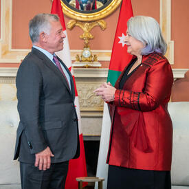 La gouverneure générale Mary Simon, portant une veste rouge, se tient debout devant le roi de Jordanie, portant une veste grise et une cravate mauve.  Ils discutent et sourient.