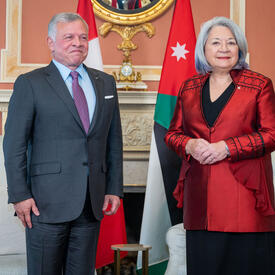 Governor General Mary Simon, wearing a red vest, is standing next to the King of Jordan, wearing a grey vest and purple tie. 
