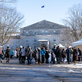 A crowd of people in front of Rideau Hall. There is snow on the ground.