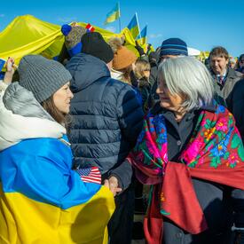 Governor General Simon speaks to a woman who has a Ukrainian flag draped over her shoulders. There is a large crowd of people behind them. Many of them are holding Ukrainian flags.
