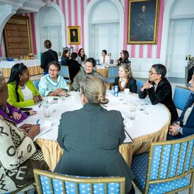 A group of women engage in conversation at a round table with Governor General Simon, in the Tent Room at Rideau Hall. 