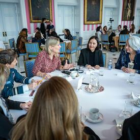 A group of women engage in conversation at a round table with Governor General Simon, in the Tent Room at Rideau Hall. 