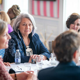 Un groupe de femmes, assises à une table ronde, discutent avec la gouverneure générale Mary Simon, dans la salle de la tente, à Rideau Hall.
