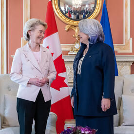 La gouverneure générale Simon se tient à côté de Son Excellence Ursula von der Leyen, la présidente de la Commission européenne. Elles sourient à la caméra. En arrière-plan, on retrouve le drapeau canadien et le drapeau européen.