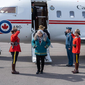Governor General Mary Simon walking outside. There is an airplane behind her.