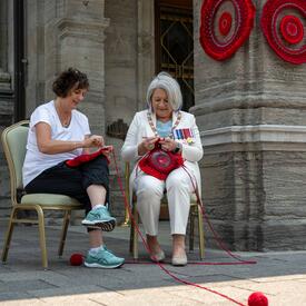 La gouverneure générale Mary Simon fait du crochet avec une autre personne. Elles sont assises à l'extérieur de Rideau Hall.