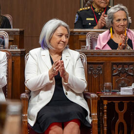 Governor General Marie Simon is seated and claps her hands