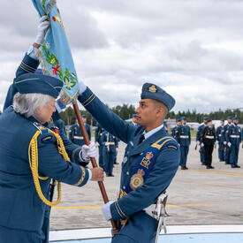 La gouverneure générale Mary Simon tient l’étendard et le remet à un membre des Forces armées canadiennes.