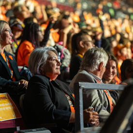 La gouverneure générale est assise dans un grand stade en présence de centaines de personnes. Beaucoup d'entre elles sont vêtues d'orange.