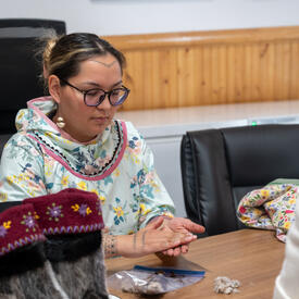 A woman seated at a table. She has something between her hands.