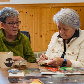 Governor General Mary Simon stitching something. She is seated at a table with another person.