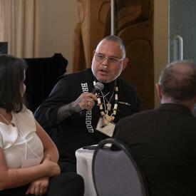 Des personnes assises à une table. Une personne tient un micro.