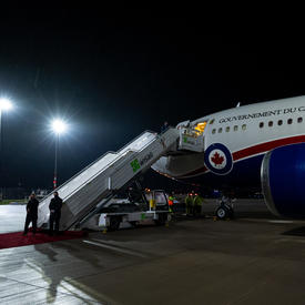 The Government of Canada plane is on the tarmac at the airport. The door to the plane is open and the stairs are open waiting for the passengers to descend. 