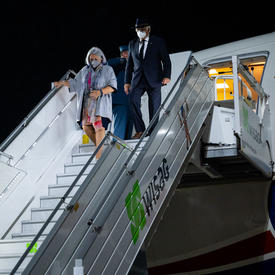 Governor General Mary Simon and Mr. Whit Grant Fraser are descending from a plane. It is nighttime.