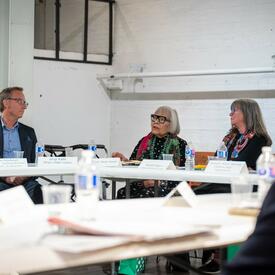 A group of people sit at a conference table in discussion. Papers and water bottles are on the table.