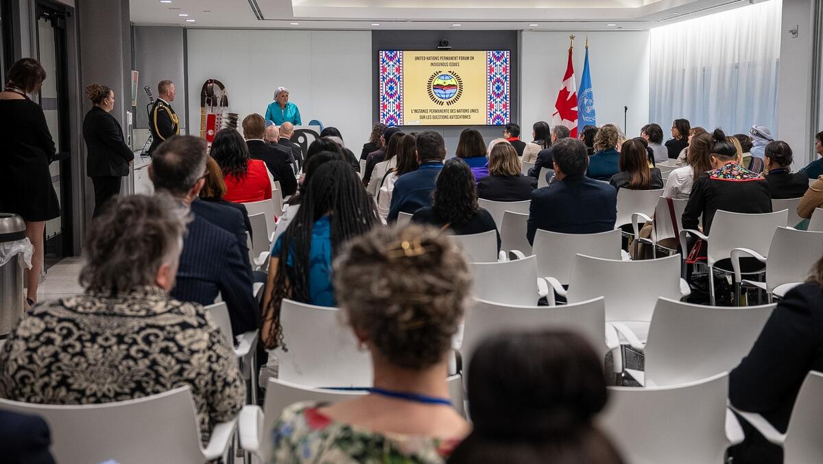 Governor General Mary Simon speaking to members of the Canadian delegation. People are seated in white chairs. A projector at the front of the room has the words "United Nations Permanent Forum on Indigenous Issues" on the screen.