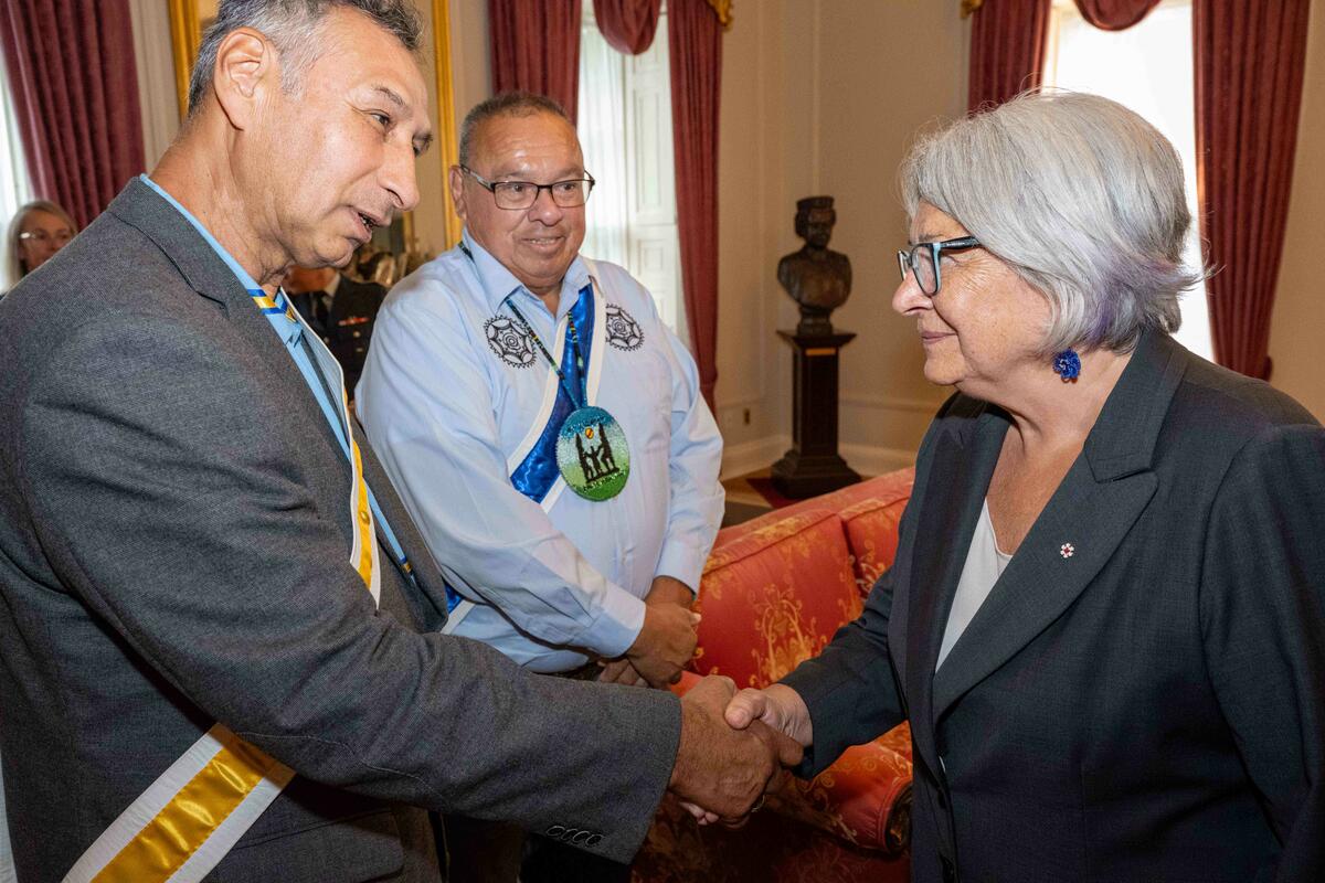 Governor General Mary Simon shakes hands with with Grand Chief Norman Sylliboy and Grand Keptin Antle Denny