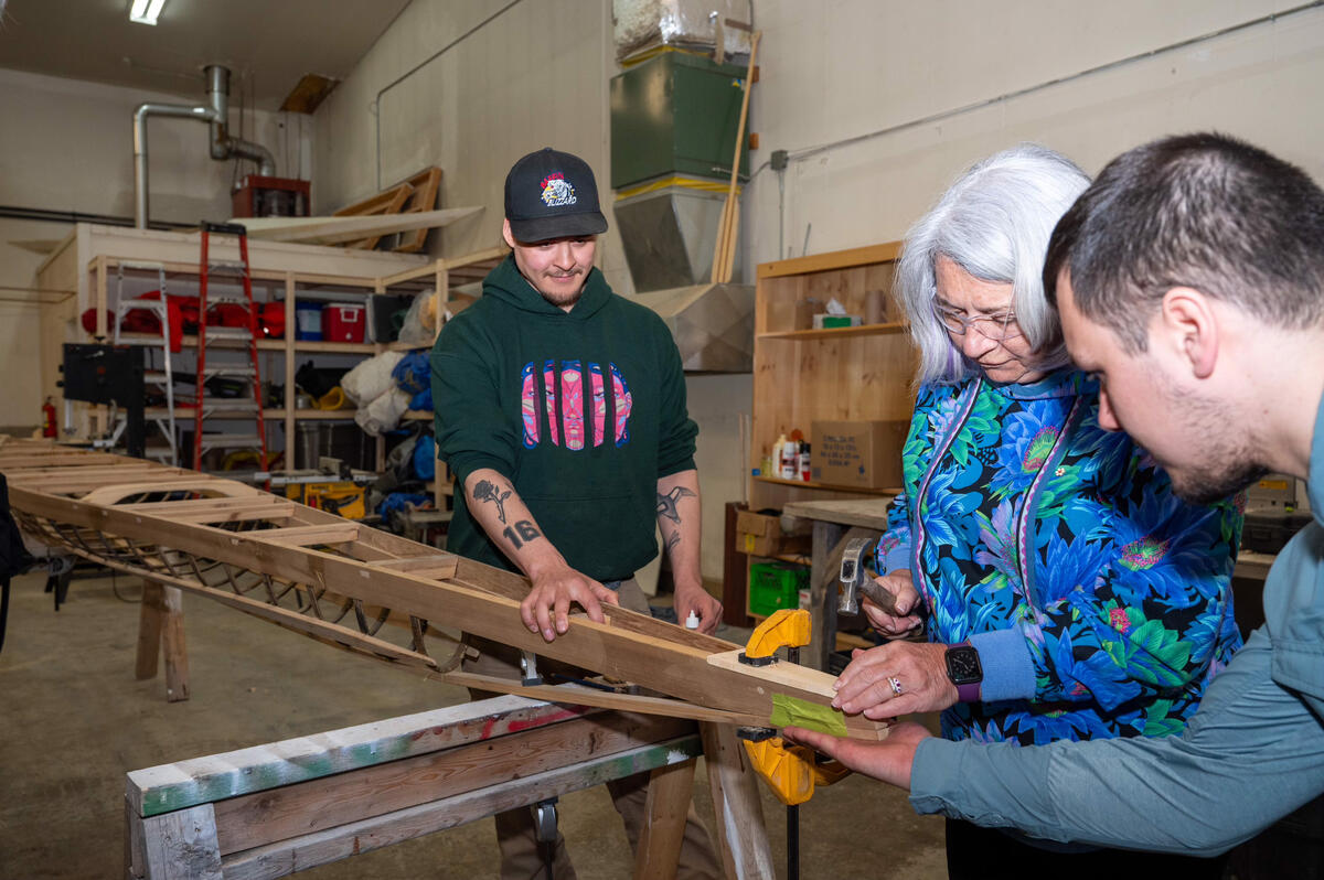 Governor General Mary Simon uses a hammer on a kayak with two members of the Qajakkut Society.