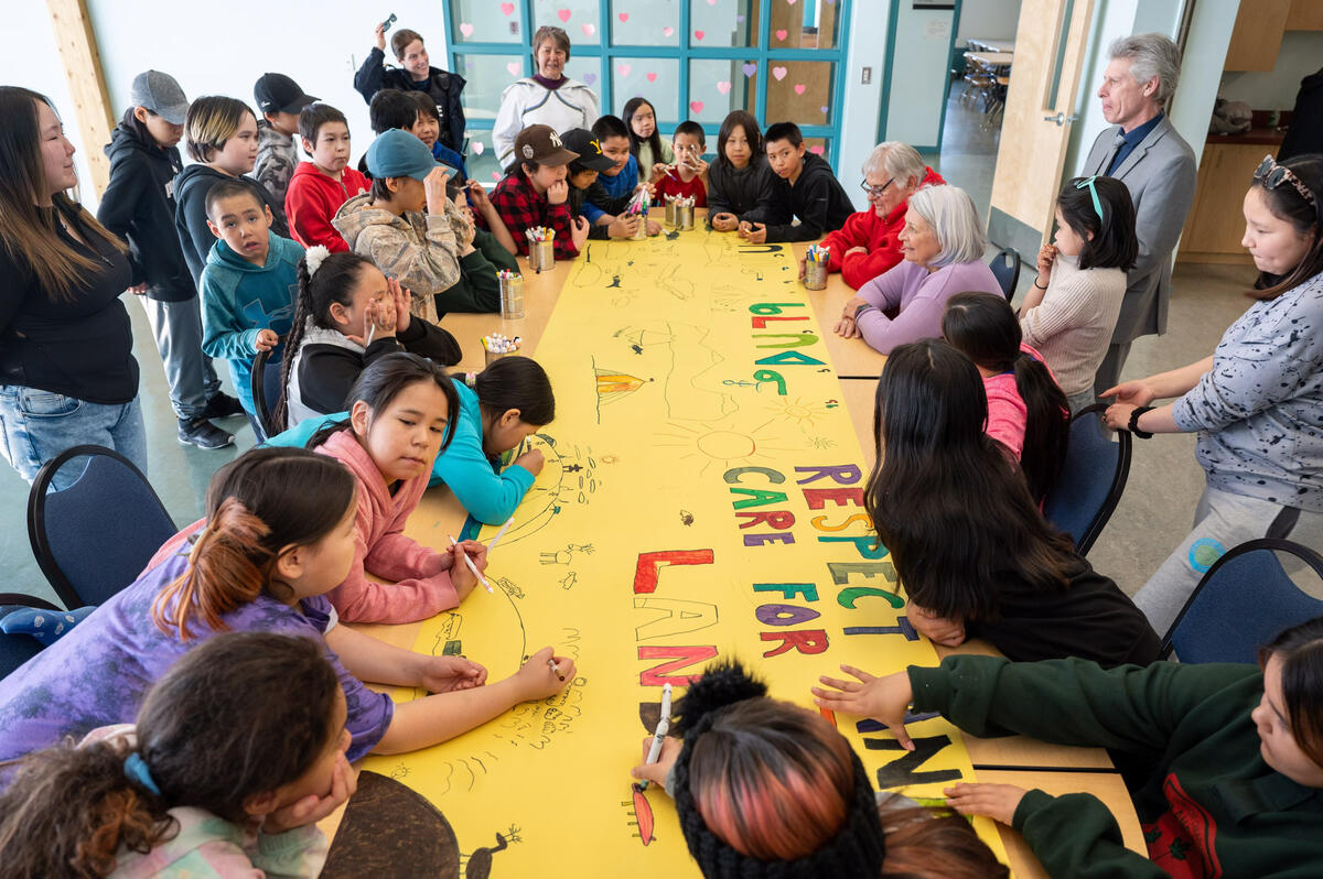 La gouverneure générale Mary Simon est assise avec des enfants pour colorier une grande bannière