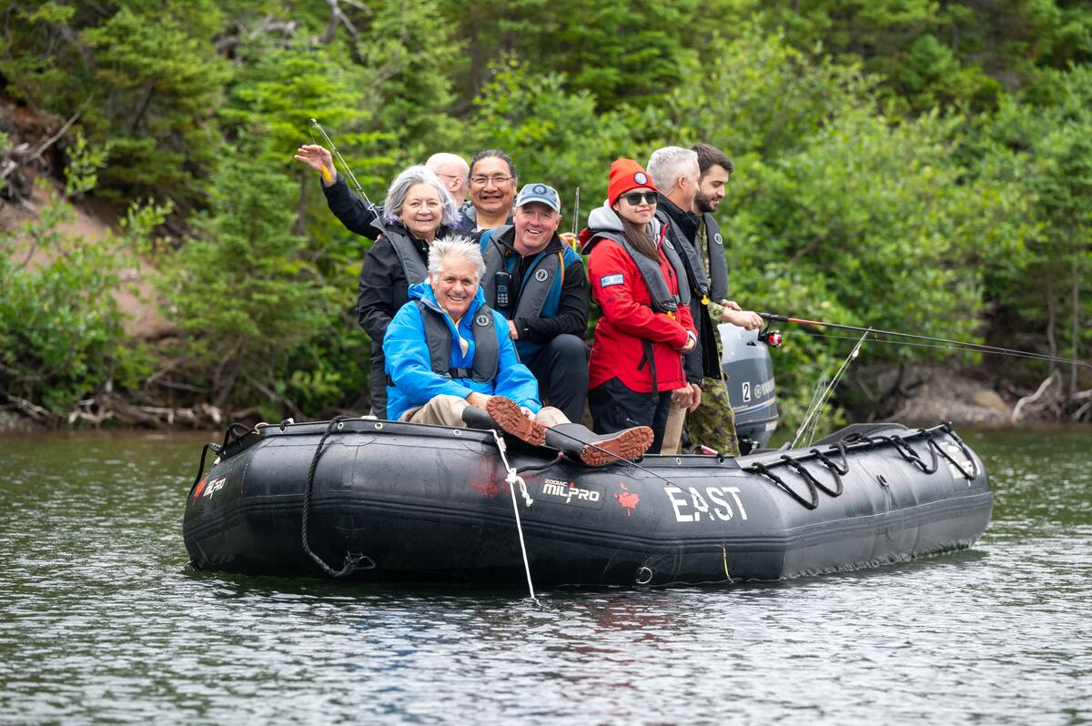 Un groupe de personnes sur un zodiac noir. Plusieurs d'entre elles sont en train de pêcher.