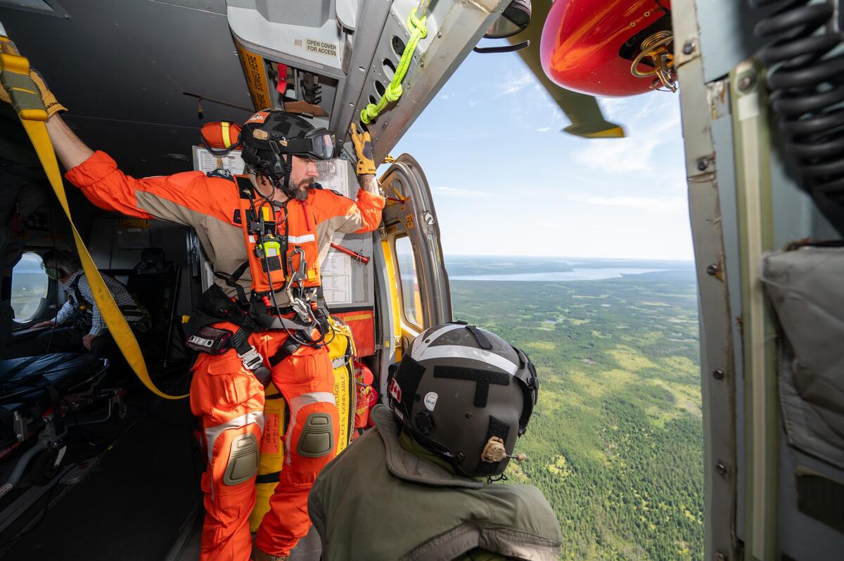 Deux membres des Forces armées canadiennes regardent depuis une porte ouverte à l'intérieur d'un hélicoptère.