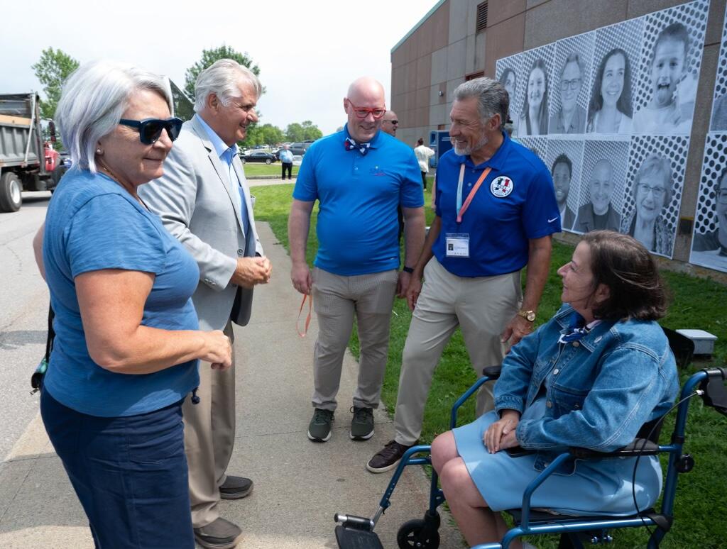 La gouverneure générale Mary Simon et M. Whit Fraser se tiennent dehors et discutent avec un petit groupe de personnes. L'une des personnes est en fauteuil roulant.