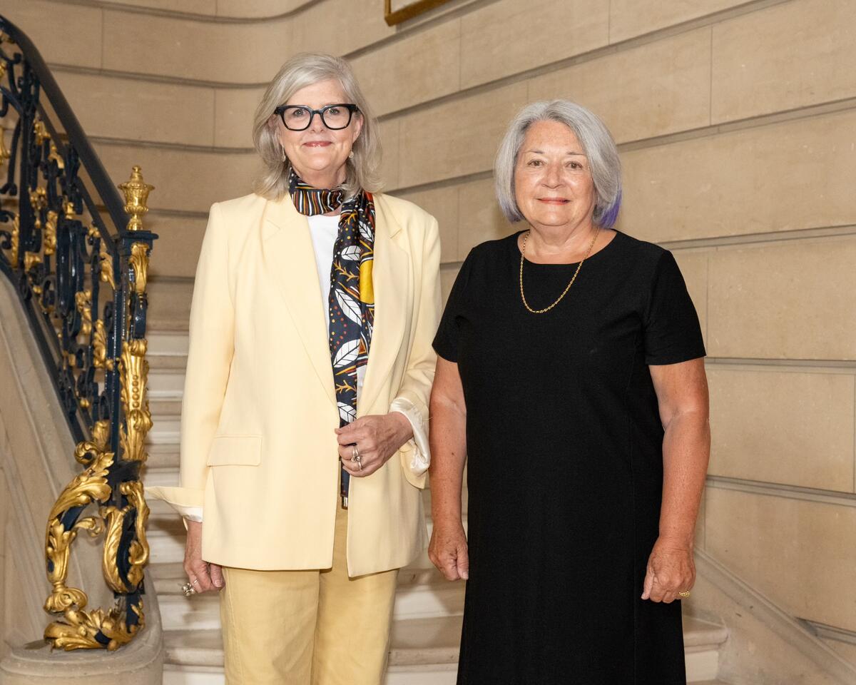 The Governor General of Australia Sam Mostyn and the Governor General of Canada Mary Simon standing on a staircase with ornate gold and black railing.  They are smilling.