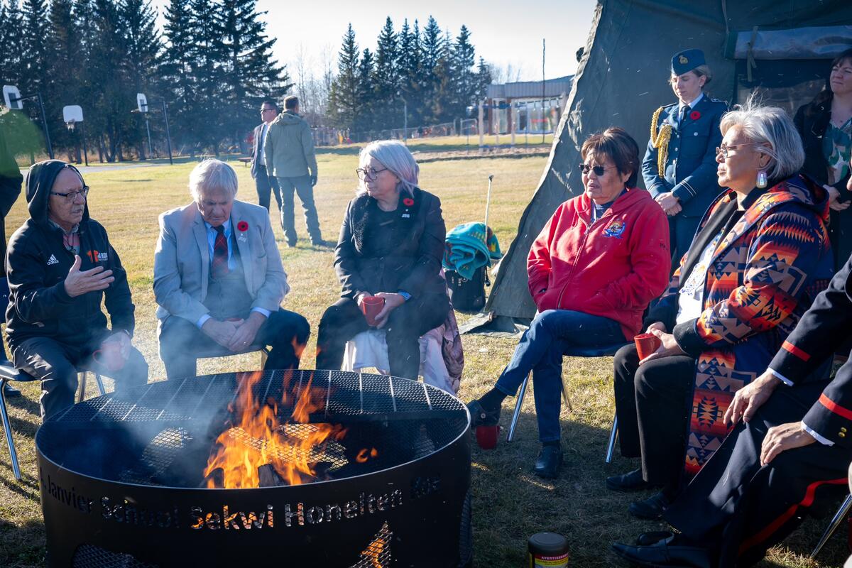 La gouverneure générale Mary Simon et M. Whit Fraser assis avec un groupe de personnes autour d'un feu en plein air
