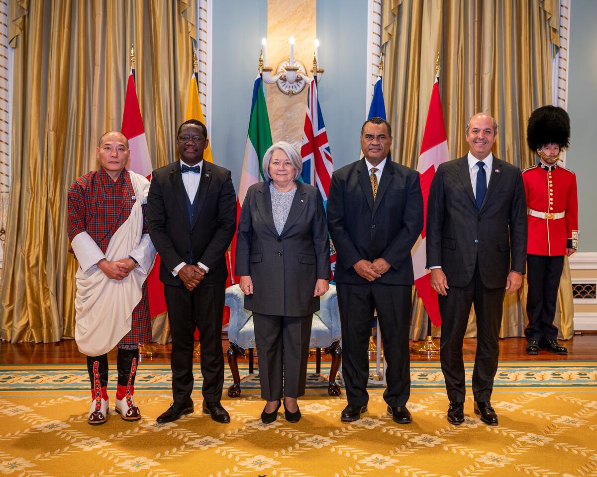 A group photo with Governor General Simon and four new heads of mission, with the flags of each country behind them. A Ceremonial Guard is in the back.