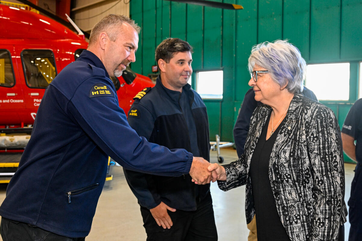 La gouverneure générale Mary Simon serre la main des membres de la Garde côtière canadienne. Un hélicoptère est visible à l'arrière-plan.