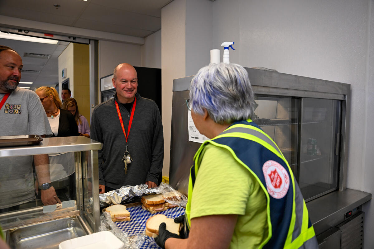 La gouverneure générale Mary Simon sert des sandwichs à des personnes dans une cafétéria. Elle porte un gilet de l'Armée du Salut.