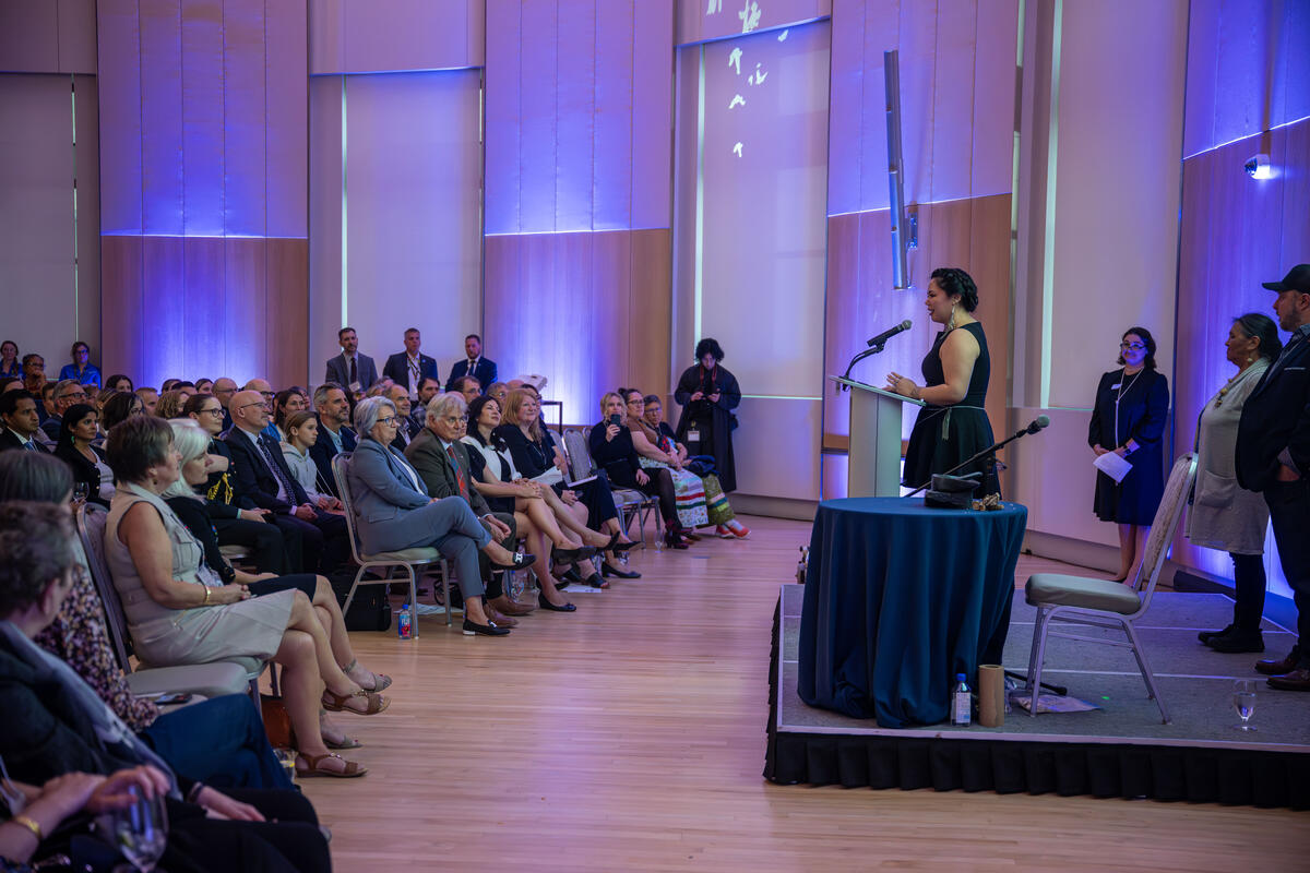 Une personne debout sur une petite estrade s'adressant à un public assis.