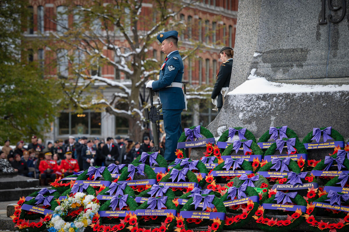 Two people in uniform stand before the War Memorial in Ottawa. Many Remembrance Day wreaths are at the base of the monument.
