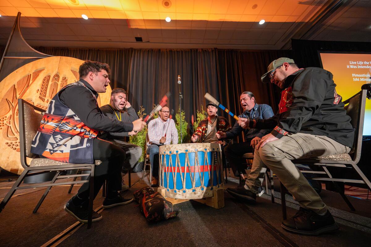 A group of performers sitting around a large drum on a stage.