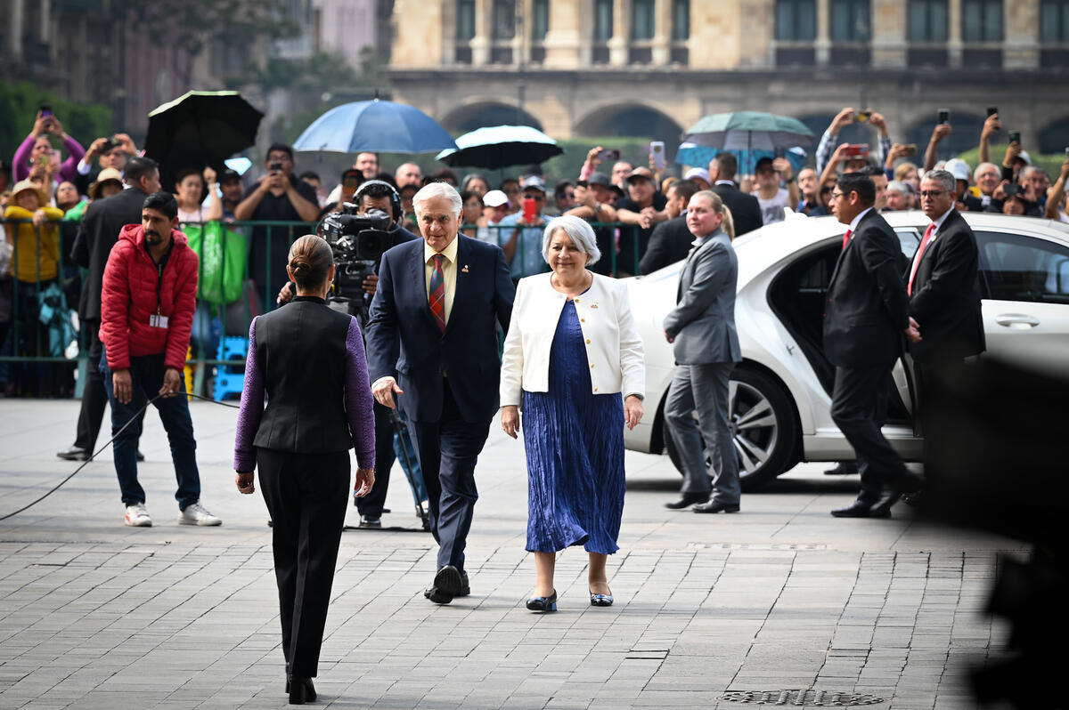 Governor General Mary Simon and Mr. Whit Fraser walking toward Her Excellency Claudia Sheinbaum Pardo, President of the United Mexican States. There is a crowd of onlookers behind barriers. Security personnel and media are present.