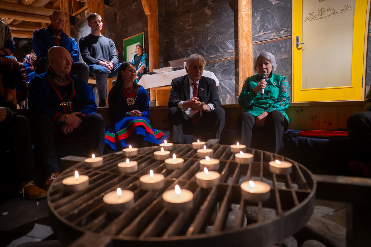 La gouverneure générale Mary Simon, assise, parle dans un micro, entourée d'un demi-cercle de personnes dans une pièce faiblement éclairée à la lueur des bougies.