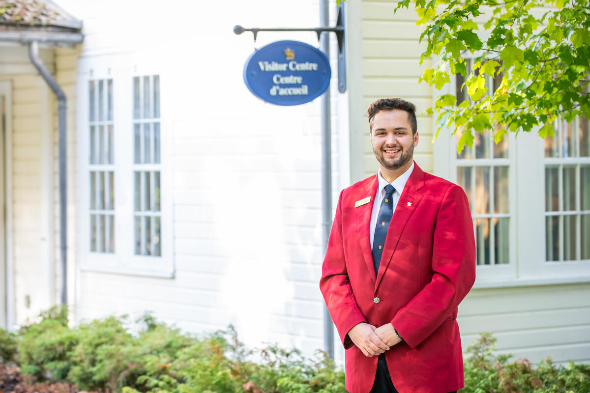 A guide wearing a red jacket standing in front of a building that has a sign 'Visitor Centre/Centre d'accueil'.