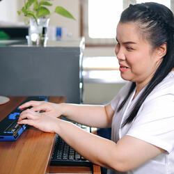 Femme asiatique atteinte de cécité utilisant un ordinateur avec un affichage braille qui peut être rafraîchit ou un terminal braille, un dispositif d'assistance technologique pour les personnes atteintes de déficience visuelle sur le lieu de travail.