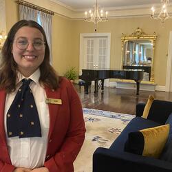 A guide smiling and standing in a fancy sitting room.