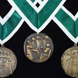Three medals on green ribbons with white borders. The medals are set on a black backdrop.