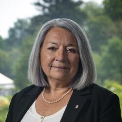Official photo of Governor General Mary May Simon. She is outdoors. The Rideau Hall gardens are visible in the background.