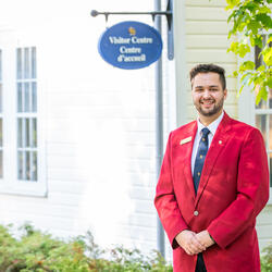 A guide wearing a red jacket standing in front of a building that has a sign 'Visitor Centre/Centre d'accueil'.