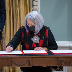 Governor General Mary May Simon is seated at a table signing a book.