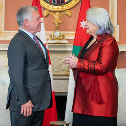 Governor General Mary Simon, wearing a red vest, is facing and talking to the King of Jordan, wearing a grey vest and purple tie. 