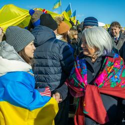 Governor General Simon speaks to a woman who has a Ukrainian flag draped over her shoulders. There is a large crowd of people behind them. Many of them are holding Ukrainian flags.