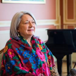 Governor General Mary Simon is sitting down. She is wearing a beautiful multi-coloured scarf. A piano is visible in the background. 