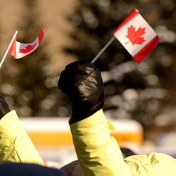 Someone holding two small Canada flags. The person is wearing black mittens and a yellow winter jacket.