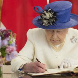 Sa Majesté la reine Elizabeth II est assise afin d'aposer sa signature à un livre.
