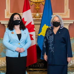 The Governor General and the President of Kosovo pose for a photo. Behind them are flags from Canada and Kosovo. Both are wearing masks.